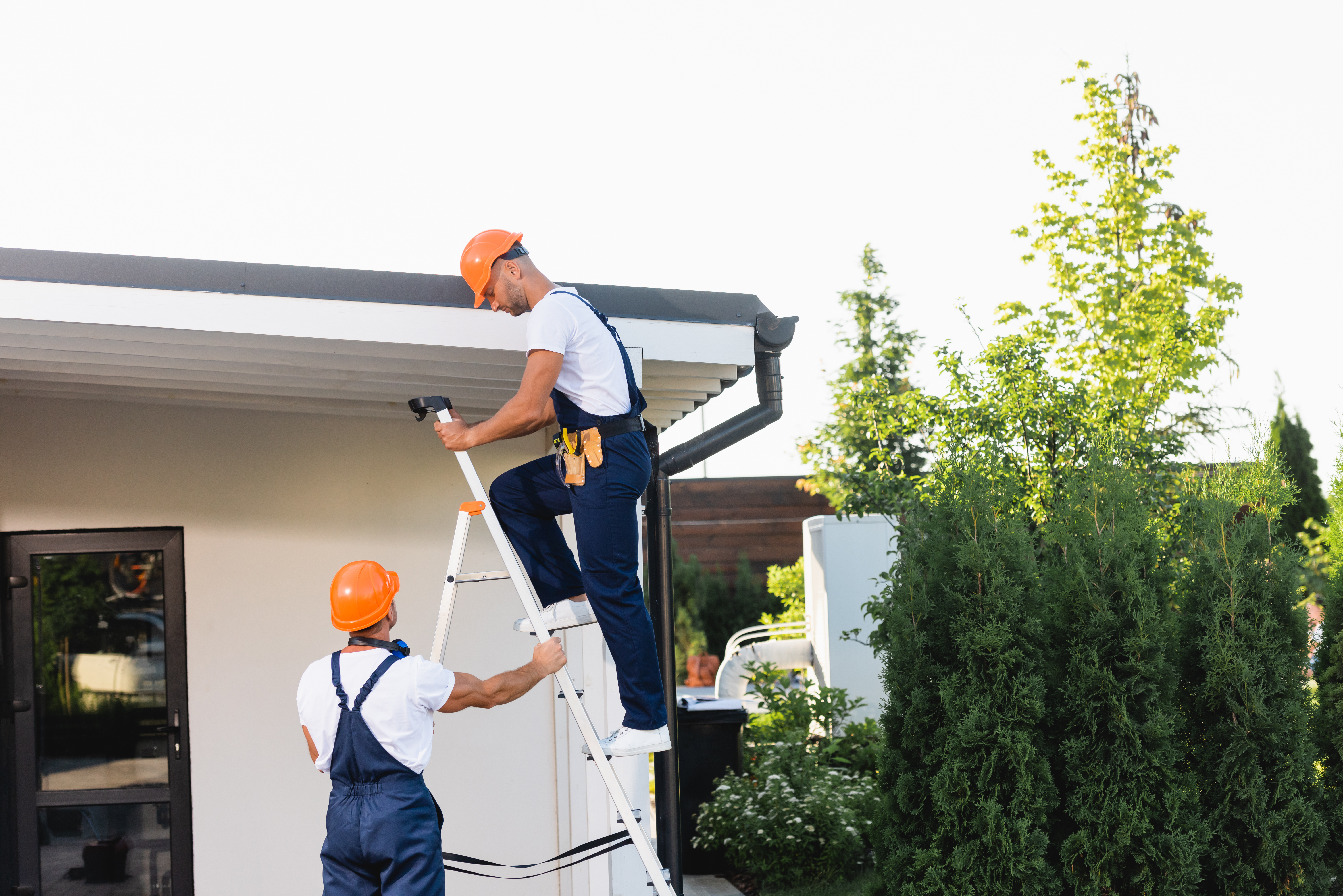 Builders using ladder near facade and roof of building on urban street